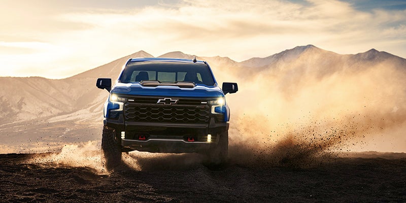 A blue truck driving on a dirt road.