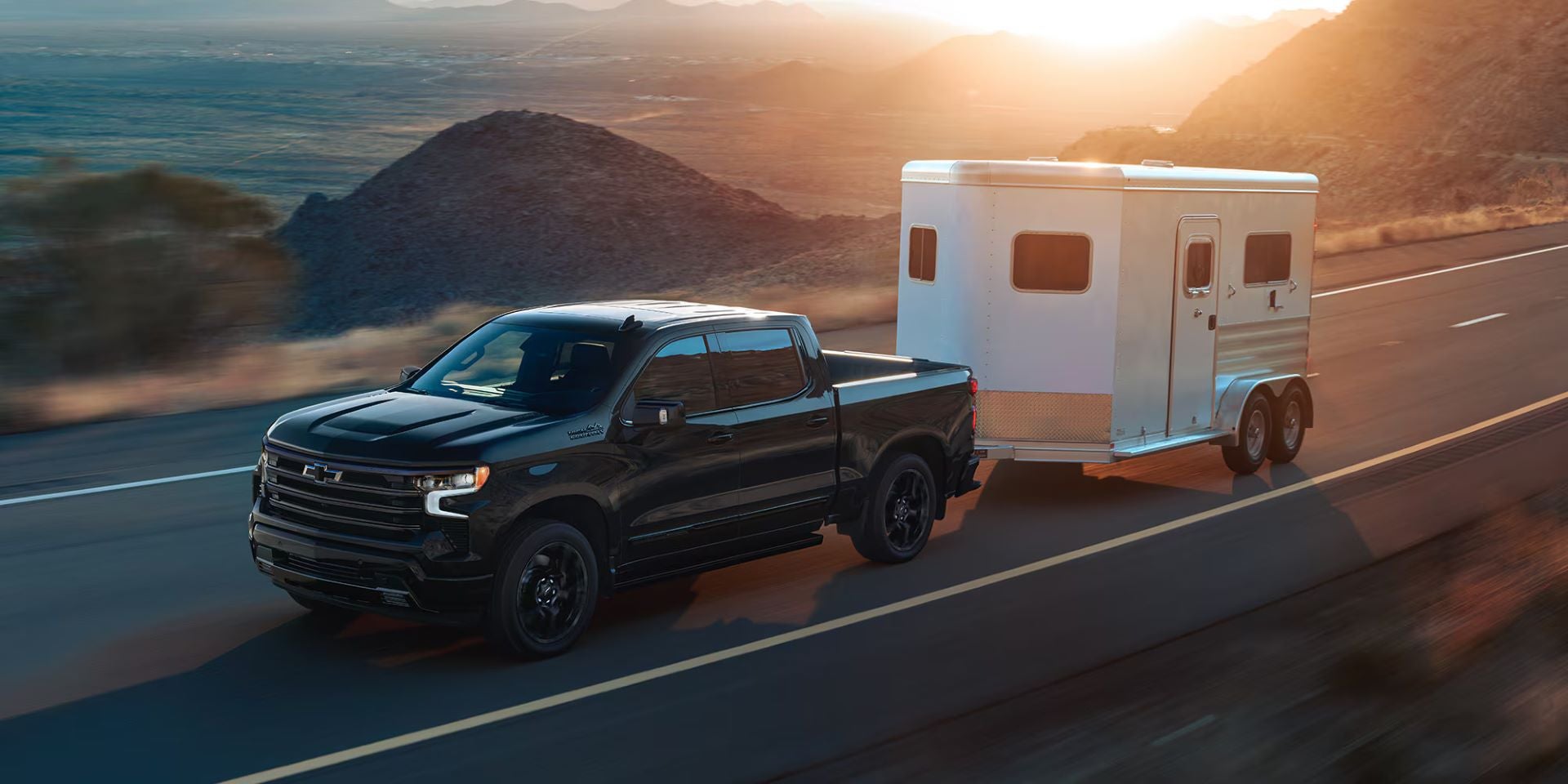 A black truck pulling a trailer on a road.