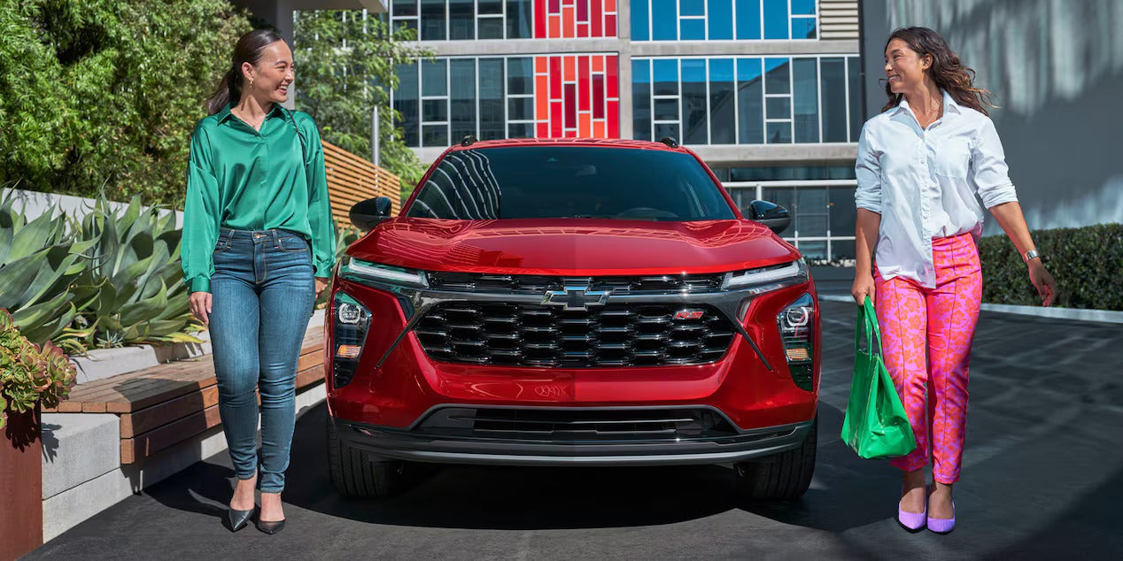 Two women walking past a red car.