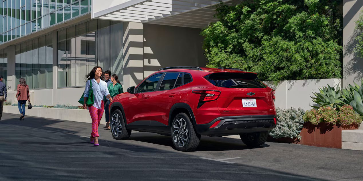 A group of people by a red car parked.